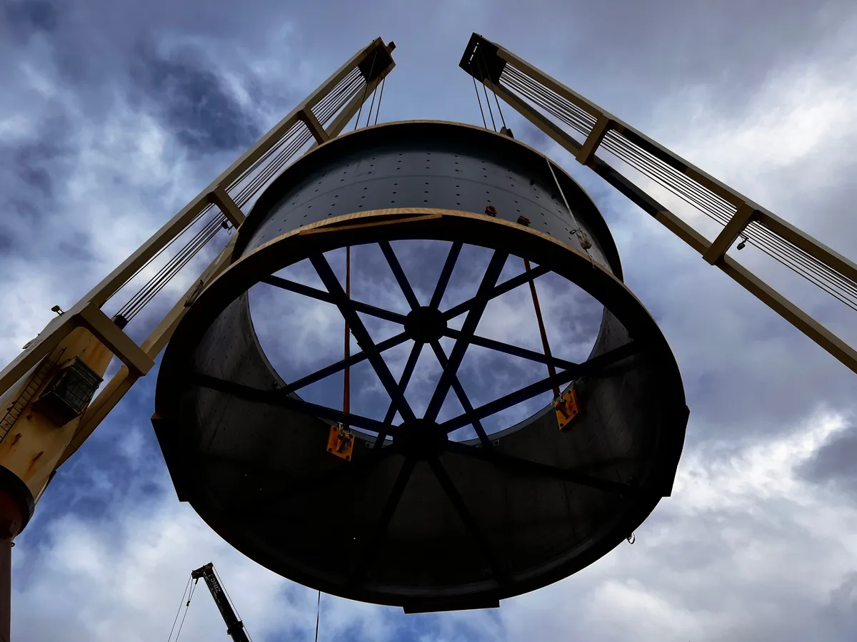 Large circular cargo suspended between twin vessel cranes